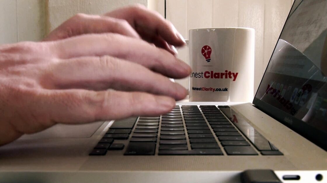 Honest Clarity brings and external perspective on charity fundraising. Closeup of man typing on laptop with Honest Clarity printed mug in background.