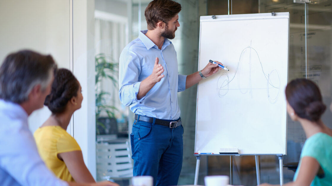 Charity CEO drawing growth line on white board and presenting to group of employees.