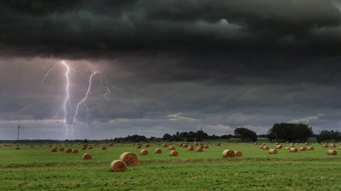 Field with hay bales. Stormy skies and lightening in the background.
